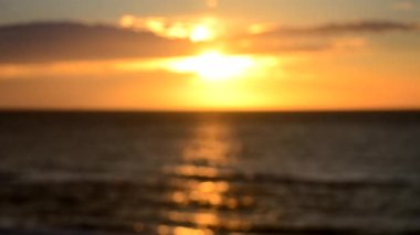 Arka plan bulanık. Güneş gün batımında bulutlarla gökyüzünde parlıyor. Gün doğumunda gün batımında. Güneşli yol, deniz dalgalarının yüzeyinde güneşli yürüyüş yolu. Güneş ışığı. Deniz manzarası. Doğal bulanık bokeh dokusu