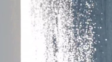 Soyut bulanık arkaplan. Deniz dalgalarının mavi yüzeyinde parlayan güneşin beyaz yansımaları. Güneşli bir günde deniz. Doğal bokeh dokusu. Dikey video