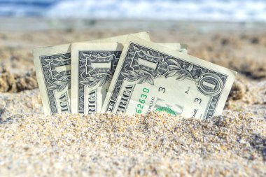 Üç kağıt para bir dolarlık banknotlar, deniz kıyısında kumlara gömülmüş. Kavram para, iş, tasarruf, mali, yatırım, nakit.
