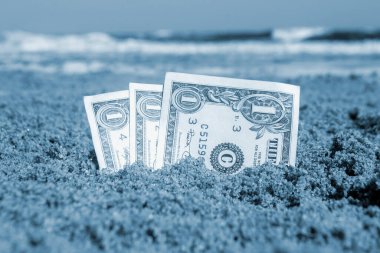 Kağıt, deniz manzaralı kumsalda gömülü bir dolarlık banknot. Güneşli bir yaz gününde kumdaki bir dolarlık nakit banknotlar. Para finans konsepti. Mavi renk