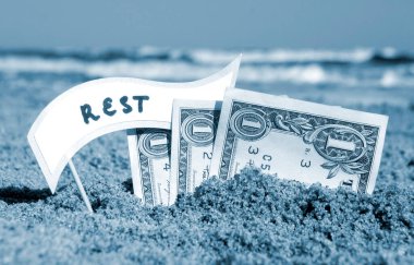 Kağıt bir dolar, kağıt konuşma balonlu küçük bir çubuk. Kum sahili arka planında güneşli yaz günlerinde deniz kenarında gömülü dinlenme. Para seyahati turizm tatili kavramı. Mavi beyaz renk