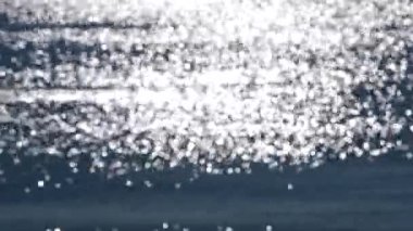 Soyut bulanık arkaplan. Deniz dalgalarının mavi yüzeyinde parlayan güneşin beyaz yansımaları. Güneşli bir günde deniz. Doğal bulanık bokeh dokusu.