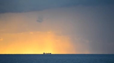 Bir tahıl taşıyıcı tanker, şafak vakti yağan yağmurlar ve büyük kara bulutlarla birlikte denizin ufuk çizgisinin çok uzağındadır. Deniz manzarası, deniz manzarası. Doğal arkaplan
