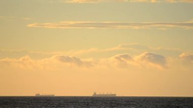 Zaman ayarlı. Denizdeki ufuk çizgisinde tanker tankerlerinin silueti ve gün batımında sarı mavi gökyüzünde hızlı hareket eden bulutlar. Deniz manzarası, deniz manzarası. Ulaşım. Doğal arkaplan