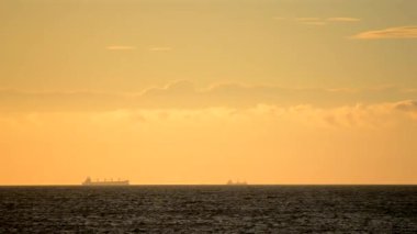 Zaman ayarlı. Denizdeki ufuk çizgisinde tanker tankerlerinin silueti ve gün batımında sarı mavi gökyüzünde hızlı hareket eden bulutlar. Deniz manzarası, deniz manzarası. Ulaşım. Doğal arkaplan