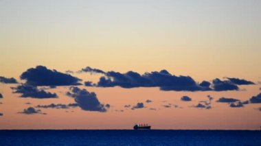 Karşıt sabah deniz manzarası. Tahıl taşıyıcısı tankeri ufuk çizgisinde denize doğru ilerliyor. Koyu mavi gökyüzü ve koyu mavi bulutlar gün batımında açık turuncu-kırmızı gökyüzüne karşı. Zaman Uygulaması