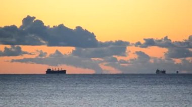 Karşıt sabah deniz manzarası. Tahıl taşıyıcı tankerler ufuk çizgisi üzerinde denize doğru ilerliyorlar. Koyu mavi gökyüzü ve koyu mavi bulutlar gün batımında açık turuncu-kırmızı gökyüzüne karşı. Zaman Uygulaması
