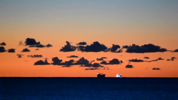 対照的な朝の海の風景 穀物運搬船は遠くの海にスカイラインに 日没の夜明けの日の出日没時に薄いオレンジ色の赤い空に対して暗い青い空と暗い青い雲日没 — ストック動画