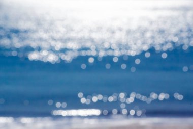 Soyut bulanık arkaplan. Deniz dalgalarının mavi yüzeyinde parlayan güneşin beyaz yansımaları. Güneşli bir günde deniz. Doğal bulanık bokeh dokusu.