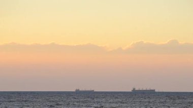 Zaman ayarlı. Denizdeki ufuk çizgisinde tanker tankerlerinin silueti ve gün batımında sarı mavi gökyüzünde hızlı hareket eden bulutlar. Deniz manzarası, deniz manzarası. Ulaşım. Doğal arkaplan