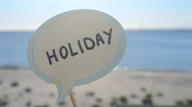Kağıt konuşma baloncuğuyla devam et. Arka planda tatil. Mavi deniz, gökyüzü, güneşli yaz gününde kumlu sahil. Mektuplardan gelen mesajlarla dolu balonlar. Konsept, sembol, tatil gezisi turizmi dinlenmesi
