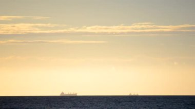 Zaman ayarlı. Denizdeki ufuk çizgisinde tanker tankerlerinin silueti ve gün batımında sarı mavi gökyüzünde hızlı hareket eden bulutlar. Deniz manzarası, deniz manzarası. Ulaşım. Doğal arkaplan