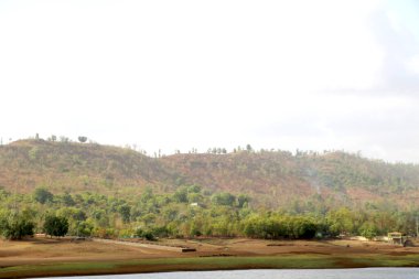Teknenin arka planında kuru arazi ve tepe ile nehir manzarası