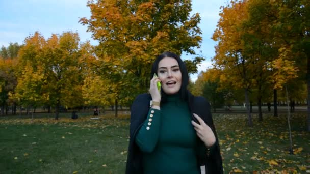 Krásná mladá brunetka žena procházky v podzimním parku a mluvení — Stock video