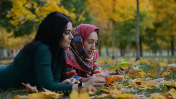 Två flickor ligger på löven med en telefon — Stockvideo