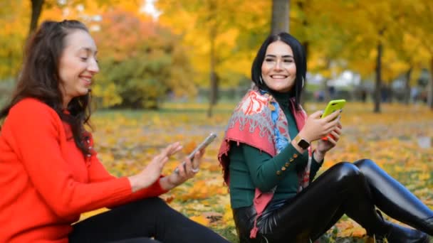Dwie szczęśliwe dziewczyny przyjazne dziewczyny siedzą w jesiennym lesie i piszą wiadomość — Wideo stockowe