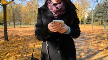 Kız akıllı telefondan mesaj yazıyor ve sonbahar parkında yürüyor.