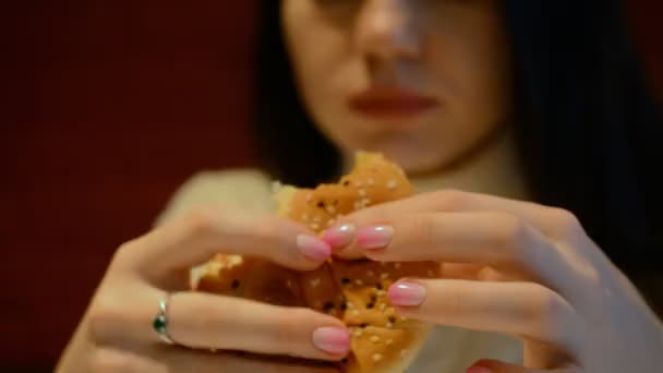 Młoda dziewczyna je hamburgera lub cheeseburgera w restauracji fast food — Wideo stockowe