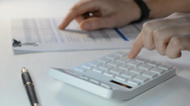 Bir muhasebecinin erkek eli hesap makinesi üzerinde çalışır ve mali bir rapor hazırlar.