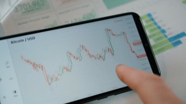 İşadamı cep telefonu ekranındaki dijital takas üzerinde Bitcoin fiyat grafiğini analiz ediyor ve öngörüyor