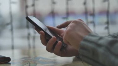 Pencerenin önündeki kafede akıllı telefonu olan bir adamın elleri ve şehir bir mesaj yazıyor.