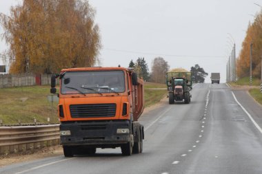 Sarı damperli kamyon asfalt yolda traktör ve sarı ağaçların arkasında sonbahar günü, Rus tarım lojistiği
