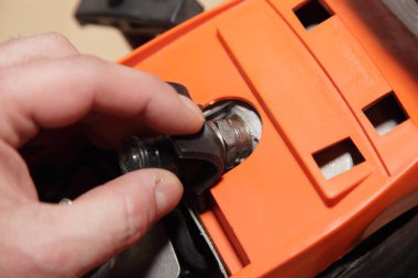 Bir adamın eli elektrikli testerenin bujisinden yüksek gerilimli kabloyu çıkarır. Yakın çekimli elektrikli aletler bakım, onarım ve tanı hizmetleri.
