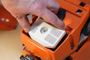 Bir adamın eli testereli hava filtresini kapağın altında tutarken, güvenlik ekipmanlarını kontrol ediyor.