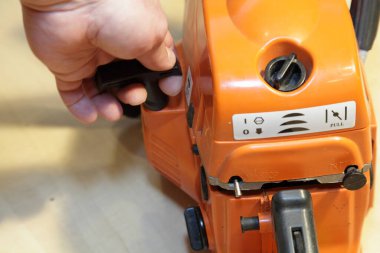 Bir adamın eli elektrikli testere motorunu manuel marş motoruyla çalıştırır. Odun kesme aletlerini tamir eder.