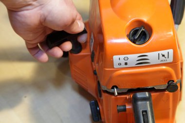 Bir adamın eli elektrikli testere motorunu elle çalıştırır. Yakın çekimde marangozluk, ahşap kesici araç gereç, motor fırlatma.