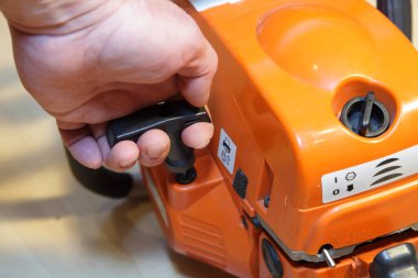 Bir adamın eli elektrikli testere motorunu elle çalıştırır. Yakın çekimde ahşap kesici aletleri kontrol eder.