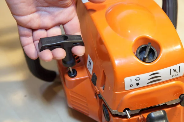 Beyaz adamın eli elektrikli testere motoru çalıştırıyor. Manüel marş kolu yakın çekimde. Tahta kesme aletleri.