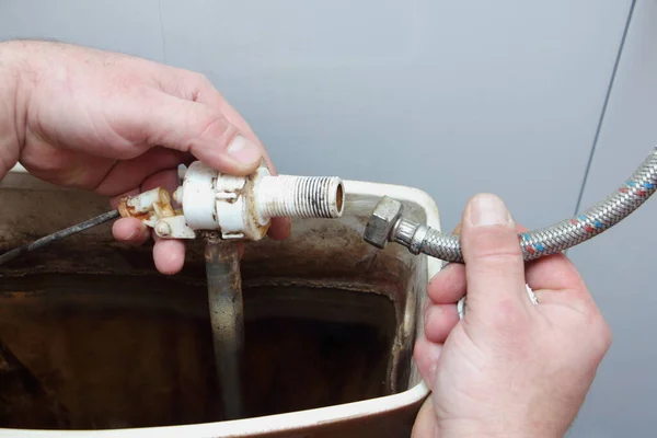 The plumber\'s hands repair the old dirty water fill valve pipe o-ring sealing in empty drain water tank closeup - DIY WC maintenance at home