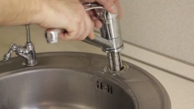 Gri paslanmaz çelikten yapılmış yumuşak boruları olan eski musluk beyaz mutfak masasında muslukçu beyaz elleriyle lavabo deliği açıyor.