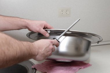 Bir adamın beyaz eli, yeni paslanmaz çelik mutfak lavabosunun kenarındaki bir dosya ile metalleri temizliyor.