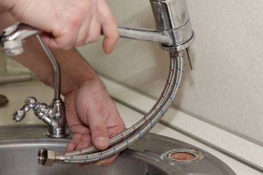 Old water tap soft pipes disassembling from gray stainless steel kitcken sink on white kitchen table with plumber white hands