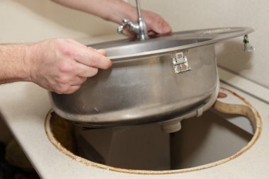 Old roung silver stainless steel kitcken sink replace on white kitchen table with plumber white hands