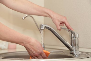 Mutfak lavabosundaki musluktan akan suyun altında beyaz kadın elleriyle sünger yıkamak.