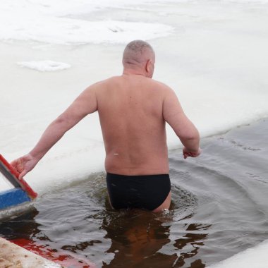 Yaşlı beyaz adam kışın bir buz deliğinde ahşap iskeleden buzlu suya girer..