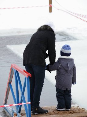 Bir anne ve çocuk kışın haç şeklinde bir buz deliğinin yanında dururlar. Hıristiyanların dini ritüeli.