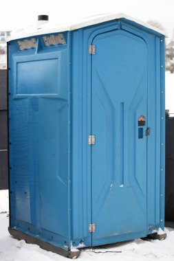 One blue moveable plastic WC cabin close up. Public toilet outdoor on snow at winter clipart