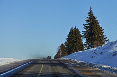Avrupa 'nın güneşli kış gününde, karlı yol kenarında daima yeşil çam ağaçları olan kurumuş, asfaltlı kırsal yol. Doğu Avrupa karayolu manzarası.