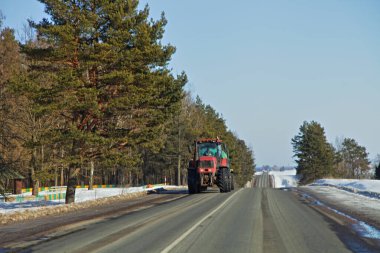 Rusya 'da banliyöde asfaltlanmış kış yolunda ağır tekerlekli traktör. Ön manzara. Avrupa 'da kırsal tarım ulaşım lojistiği.