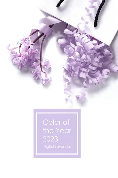 White gift box with spring pink lilac flowers and lavender serpentine on white background. Concept of trendy lavender color. Text Color of the year 2023 Digital Lavender