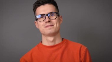 Gri arka planda gözlüklü genç bir adamın portresi.