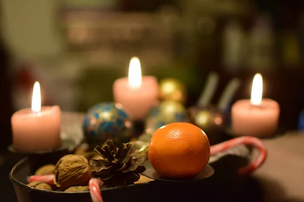 Tres velas encendidas con un manadarín y un cono de pino como decoración navideña —  Fotos de Stock