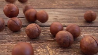 Kabuklu Macadamia fındıkları eski ahşap şarap tahtasına düşer. Yavaş çekim.