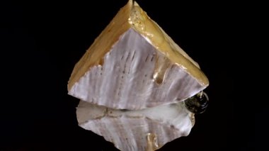 Brie peynirinden damlayan bal damlaları aynalı siyah arka planda.