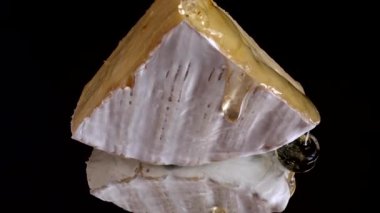 Brie peynirinden damlayan bal damlaları aynalı siyah arka planda.