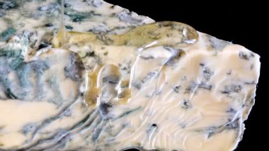 Dorblu peynirinden akmakta olan bal damlaları aynalı siyah arka planda.